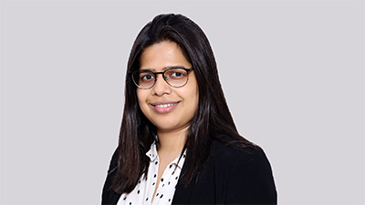 Palak Jain, a person with long straight dark hair wearing glasses and a black jacket over a white collared shirt with black polka dots.